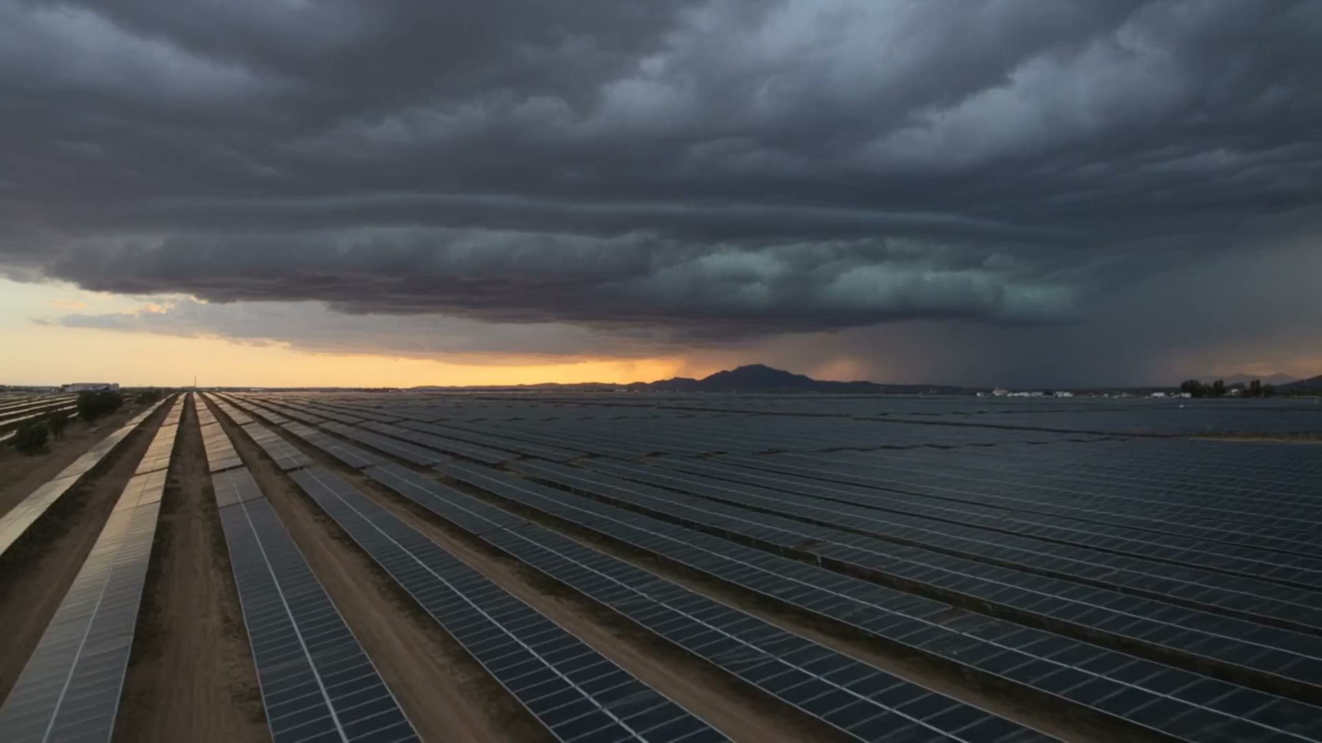 Cinematic aerial view of a utility-scale solar array and transmission corridor at dawn, representing Ampiria's regional infrastructure platform